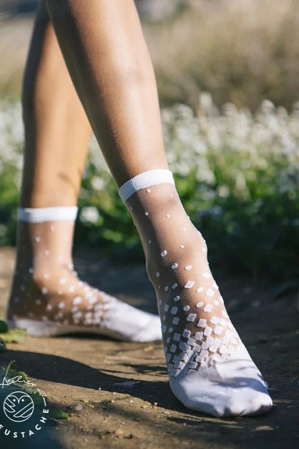 Sheer white ankle socks with polka dot pattern outdoors on a sunny day