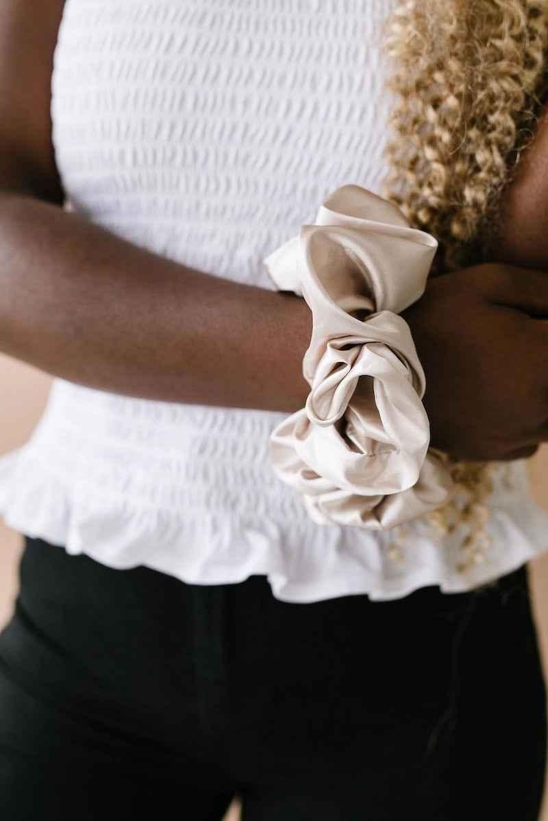 Woman wearing large satin scrunchie on wrist, styled with white smocked top, Love Classic