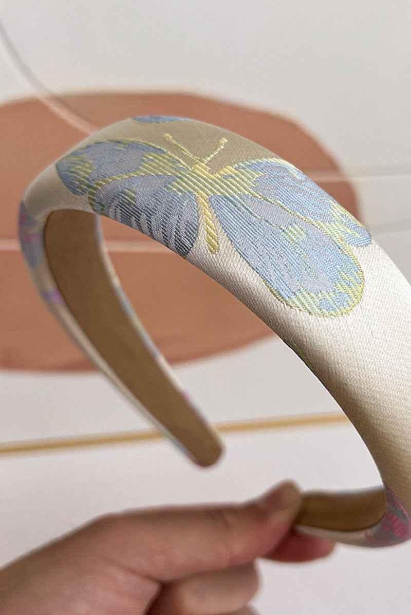 Love Classic padded headband with blue butterfly embroidery, held in hand against neutral background