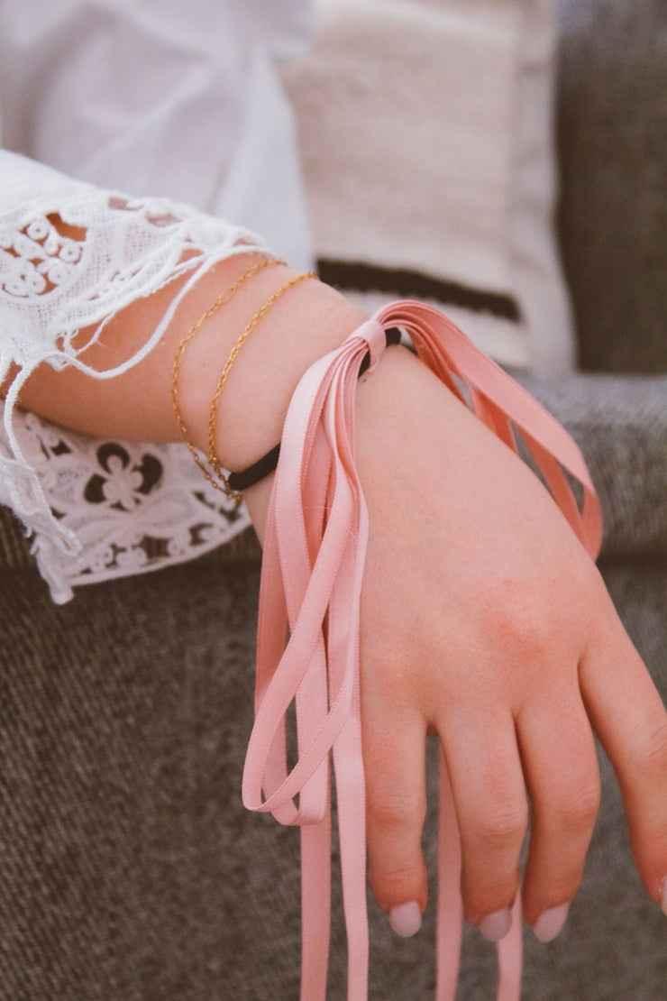 Woman wearing gold bracelets and a pink ribbon bow on wrist, Love Classic fashion accessory