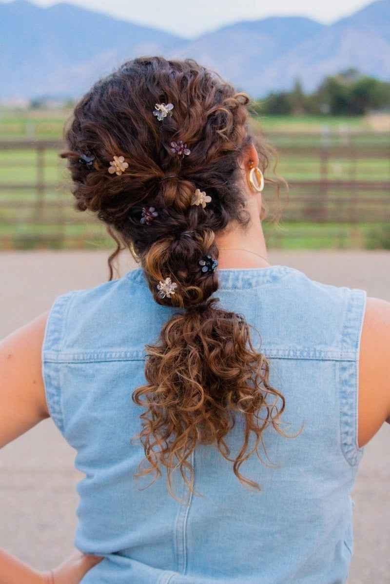 Curly braided hair with decorative flower clips, outdoor setting, Love Classic style inspiration