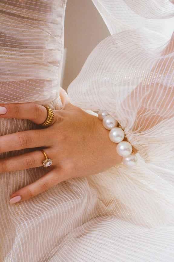 Elegant hand with gold rings and pearl bracelet on pleated white dress, Love Classic style