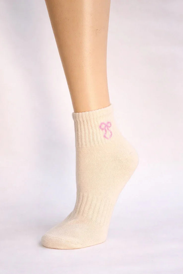 Ivory ankle sock with pink bow embroidery, soft knit, modeled on a leg against white background.