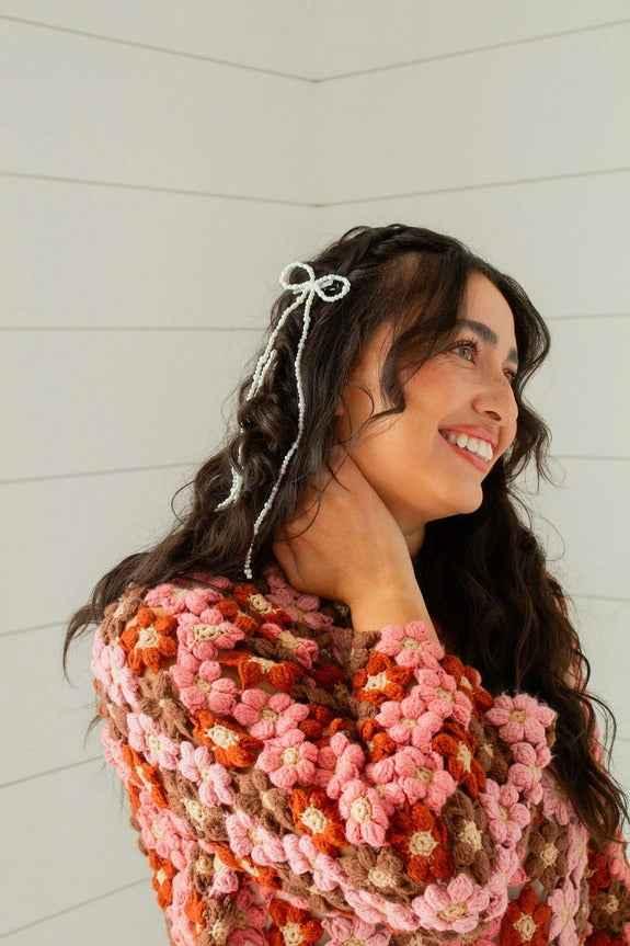 Smiling woman in a colorful crochet sweater with braided hair and a bow, Love Classic style