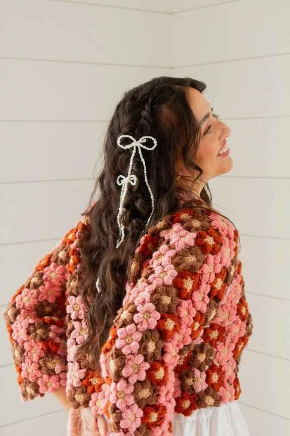 Smiling woman in a floral crochet sweater with braided hair and bows, Love Classic style