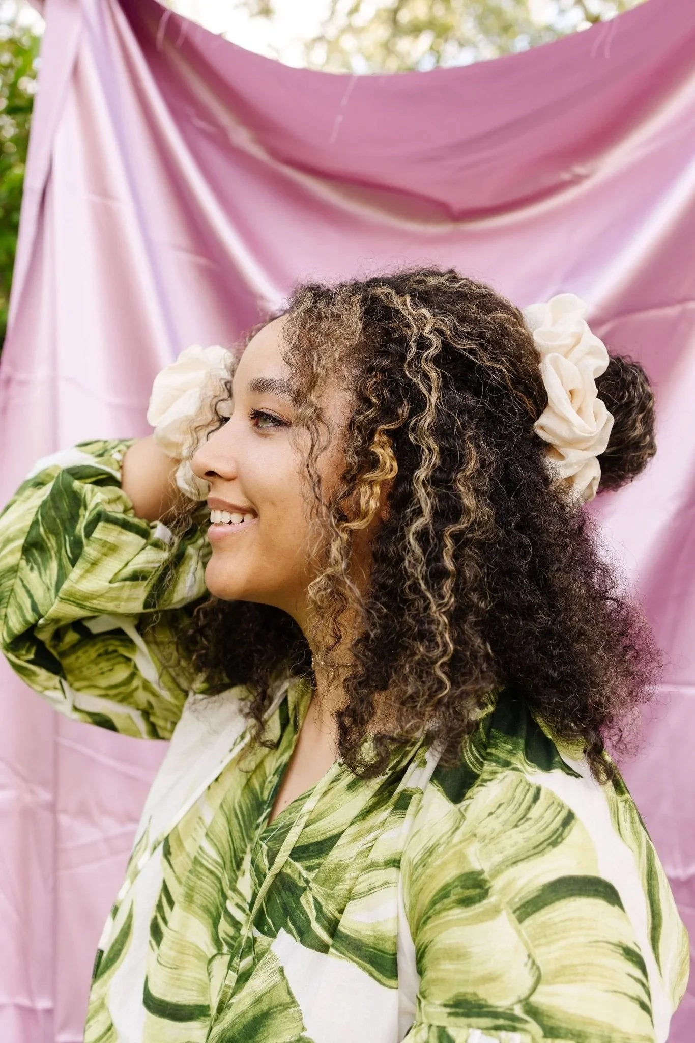 Woman with curly hair wearing a cream jumbo scrunchie, green leaf top, pink backdrop, Love Classic