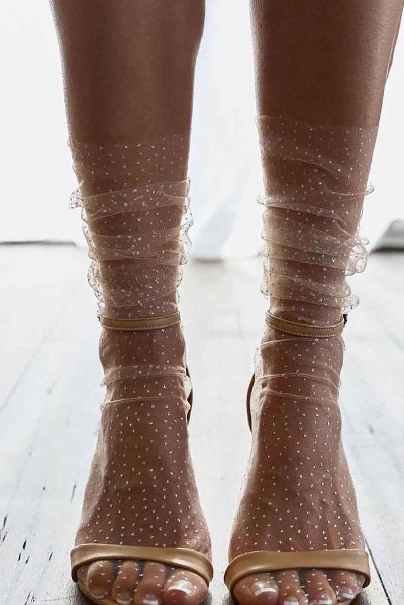 Sheer polka dot socks with ruffled trim styled with open-toe sandals on wooden floor