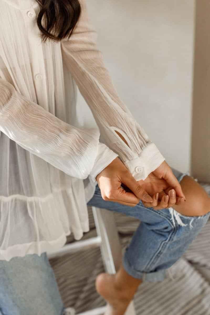 Woman wearing sheer white blouse and blue jeans from Love Classic clothing