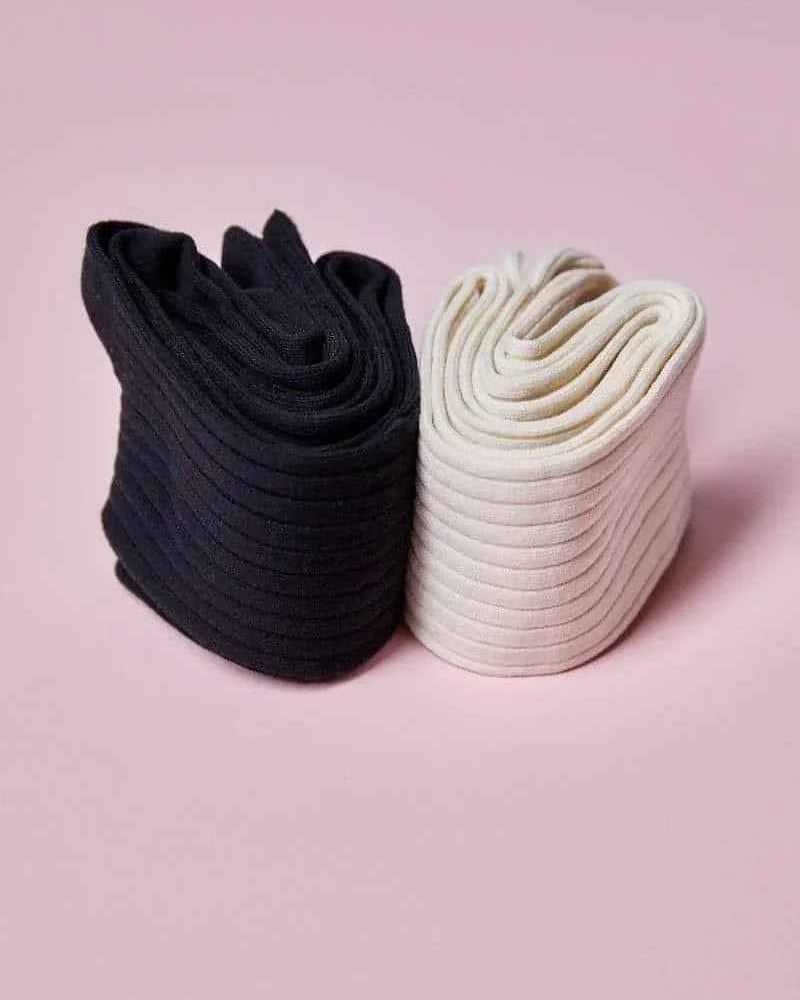 Two pairs of folded ribbed socks, one black and one white, on a pink background from Love Classic