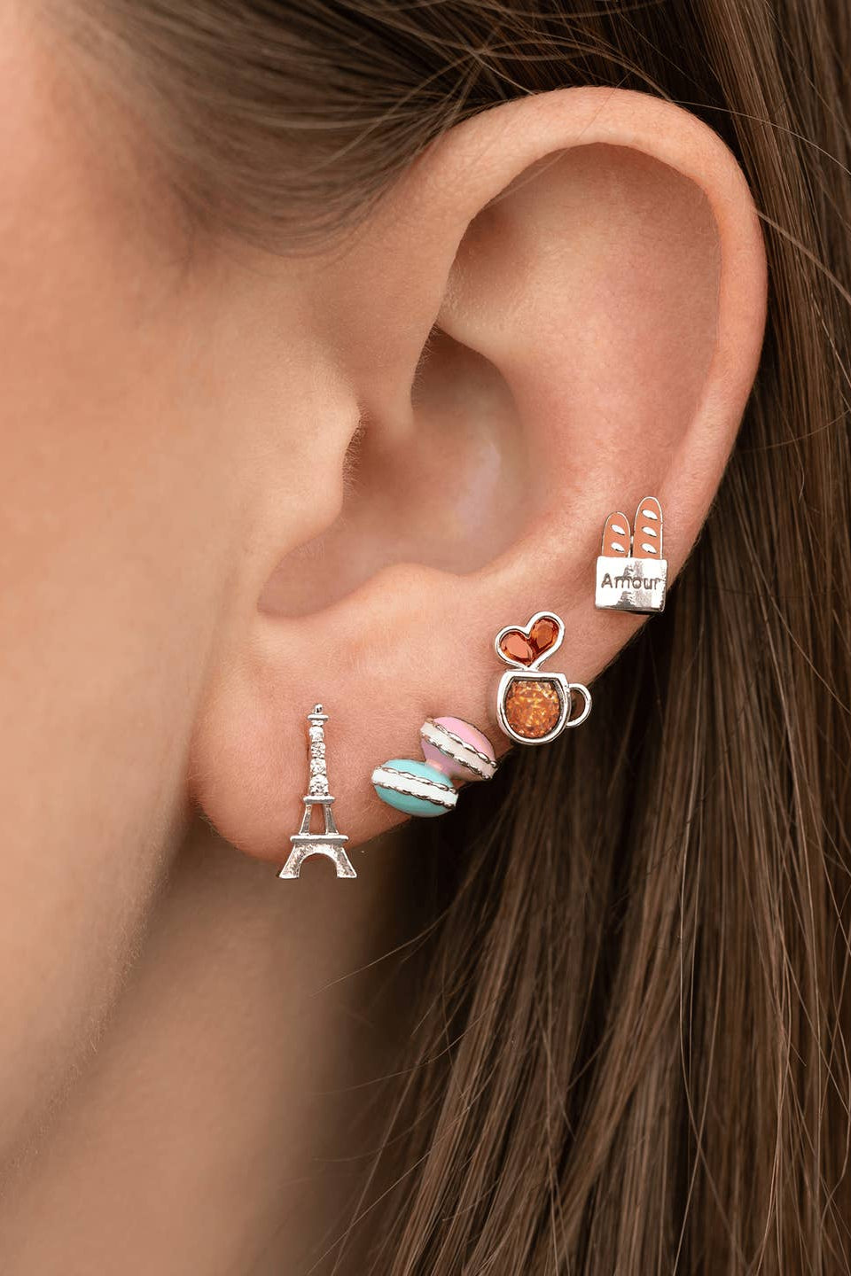 Café de Paris Stud Set, model wearing selected Paris inspired studs in a layered ear stack featuring Eiffel Tower, macarons, coffee cup, and baguette shapes.