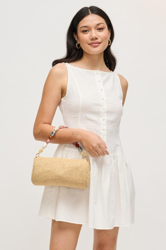 Model pairing the natural Rachel Straw Clutch with a day-to-night look, featuring a handwoven exterior, sculpted bead trim, and metallic hardware.