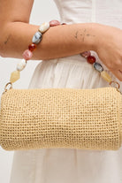 Close-up image of model carrying the natural Rachel Straw Clutch highlighting the intricate straw weave, dimensional bead details, and refined metal hardware.