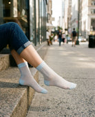Soft Horizon Sheer Socks featuring a fine sheer ribbed texture with contrast heel, toe, and cuff accents, worn with rolled jeans while seated outdoors, highlighting a soft fit and relaxed city style.