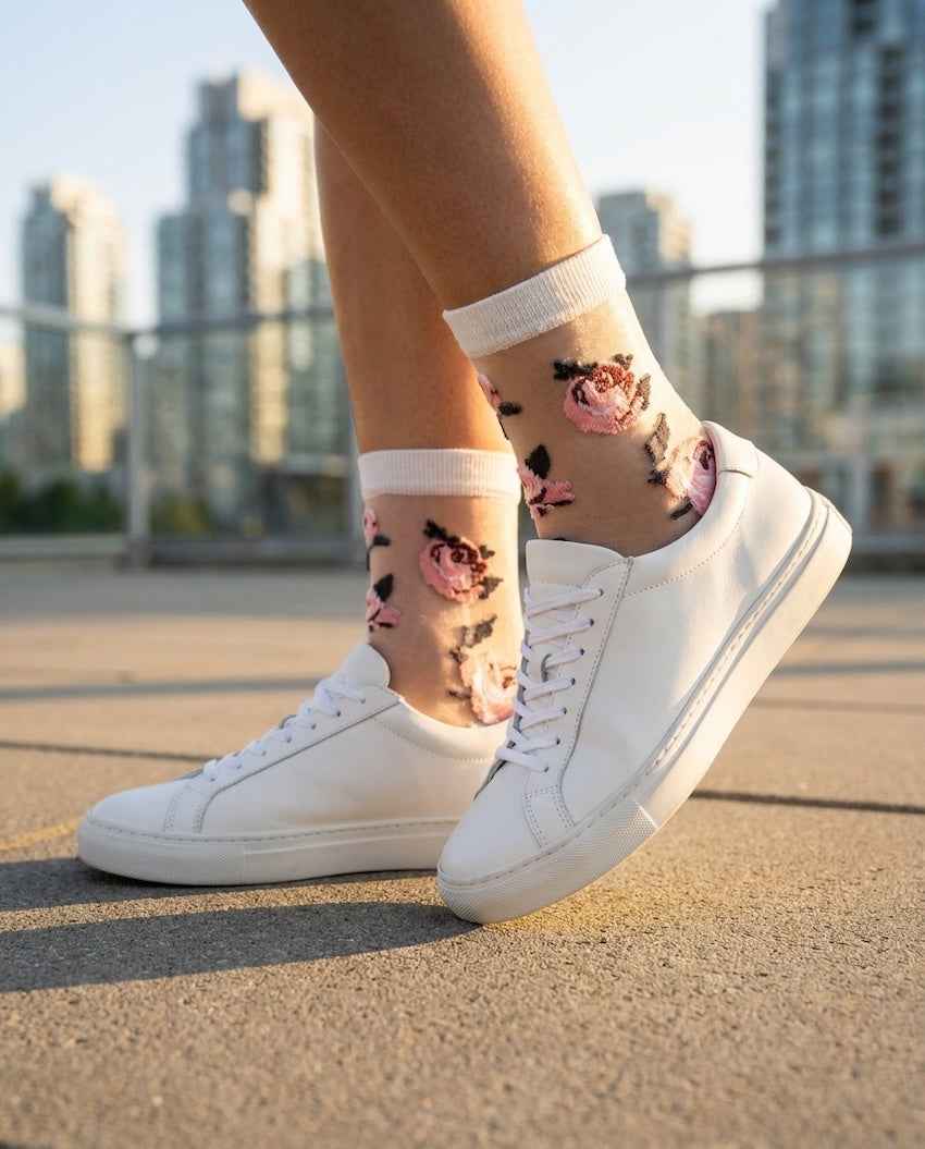 Roses Sheer Socks 2-Pack featuring sheer ankle socks with raised rose embroidery and soft ribbed cuffs, worn with white sneakers in an outdoor city setting, highlighting the delicate floral pattern and light transparent texture.