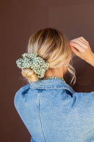 Model wearing the Lindsey Checked Jumbo Scrunchie featuring a green and white checkered pattern with soft crushed polyester texture for a festive hairstyle accent.