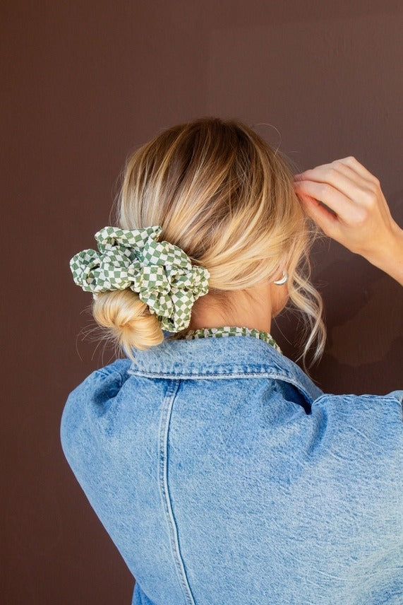 Model wearing the Lindsey Checked Jumbo Scrunchie featuring a green and white checkered pattern with soft crushed polyester texture for a festive hairstyle accent.