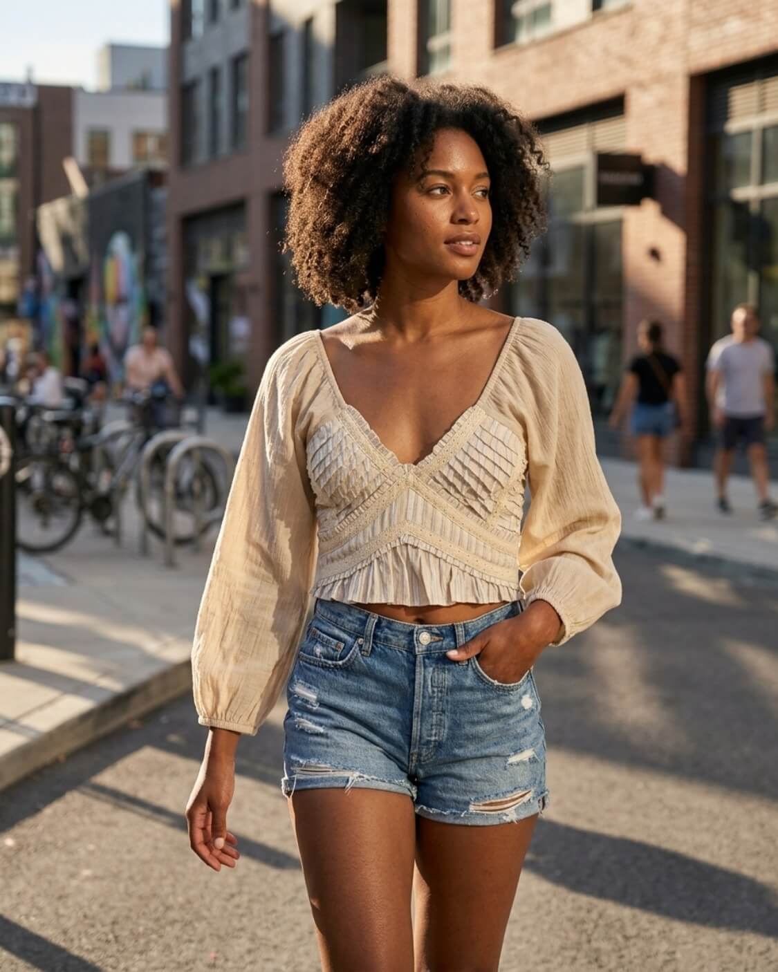 Tied To You Top featuring a cropped fit with a deep V neckline, pleated front panels, long puff sleeves, and a ruffled hem, worn with denim shorts on a city street, highlighting the textured bodice and relaxed warm-weather styling.
