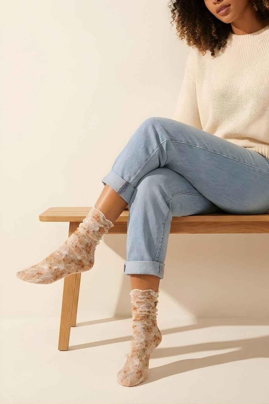 Floral mesh sheer socks in orange with delicate lace overlay and soft floral print, styled with rolled cuff jeans and a knit sweater while seated on a wooden bench, highlighting the lightweight, semi-transparent fabric and feminine design.