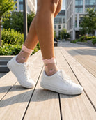 Whimsical Ruffle Edge Sheer Socks featuring a transparent ankle-length silhouette with delicate ruffle trim and playful peach motifs, worn with white lace-up sneakers while walking along a sunlit urban boardwalk, highlighting lightweight comfort and charming everyday styling.