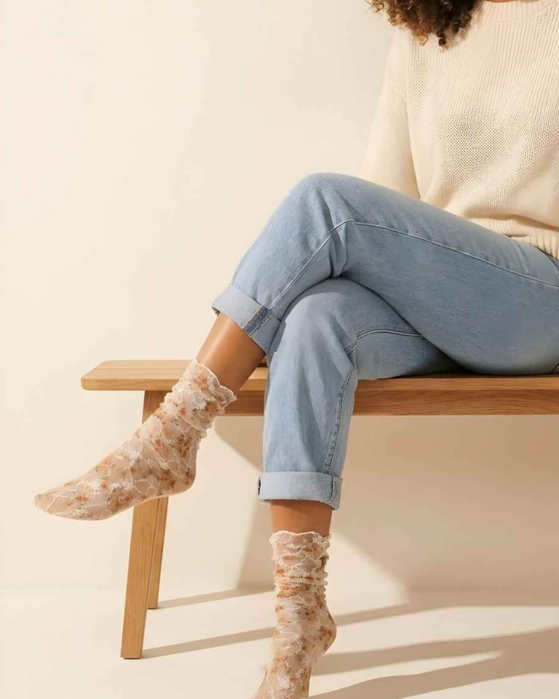 Floral mesh sheer socks in orange with delicate lace overlay and soft floral print, styled with rolled cuff jeans and a knit sweater while seated on a wooden bench, highlighting the lightweight, semi-transparent fabric and feminine design.