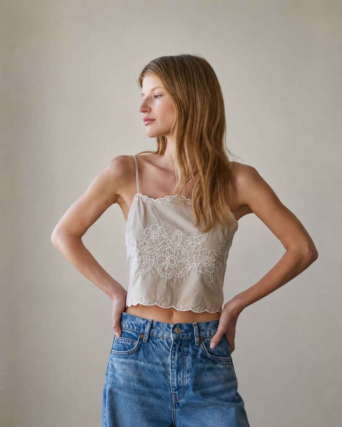 Floral Lace Work Sleeveless Top featuring delicate floral embroidery with scallop edge trim and slim spaghetti straps, worn with relaxed wide leg denim while posing with hands at the waist in a softly lit studio, highlighting the lightweight cropped silhouette and feminine detailing.