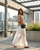 Chiffon Wide Leg Pant featuring a flowing wide-leg shape with soft pleated movement and a relaxed full-length fit, styled with a lightweight top and sandals on a city terrace, highlighting airy movement and easy everyday styling.