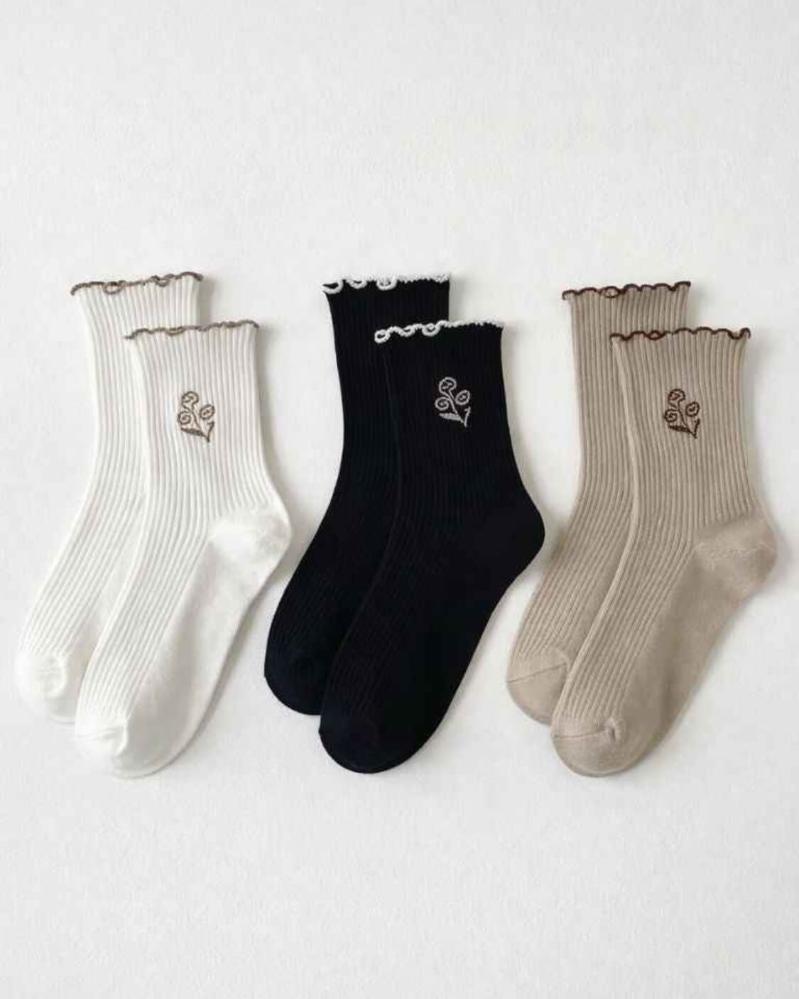 3-Pack Floral Bloom Ribbed Ruffle Crew Socks featuring three assorted ribbed crew sock pairs with scalloped ruffle cuffs and floral embroidery accents, arranged flat against a clean studio background, highlighting soft texture, ankle coverage, and everyday styling variety.