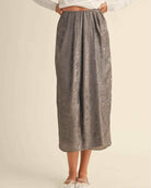 Metallic Fabric Pleat Detailed Skirt featuring a full length flowing structure with soft pleated detailing and metallic inspired texture, styled with ballet flats against a minimal neutral backdrop, highlighting effortless drape and understated sophistication.
