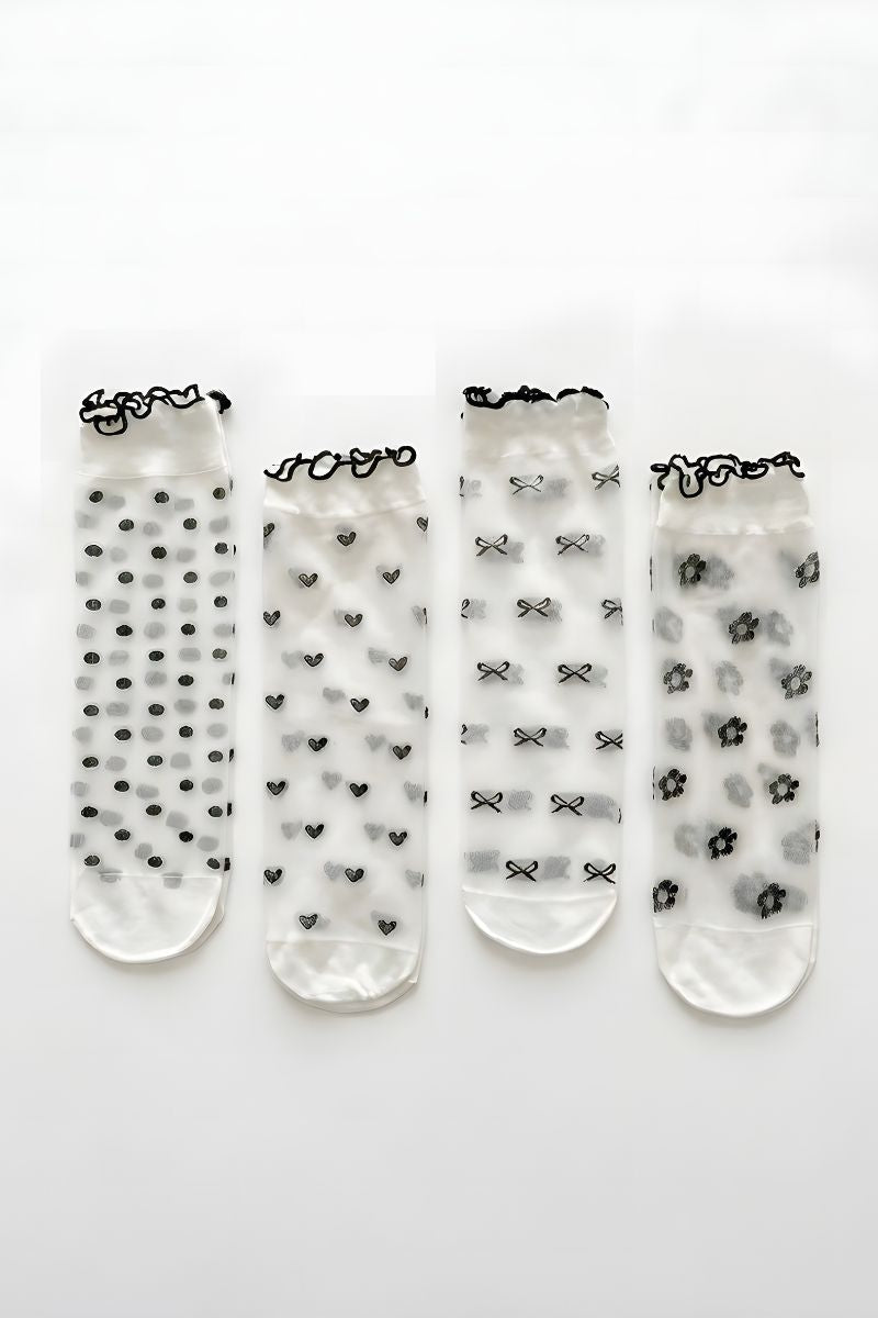 Bundled Pack Geo Print Ruffle Edge Sheer Socks featuring a transparent lightweight finish with delicate ruffle trim cuffs and assorted black geometric patterns including dots, hearts, bows, and florals, displayed laid flat in a row on a clean white background to highlight variety and subtle texture.