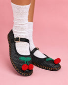 Cherry Accent Mary Jane Flats, black woven Mary Jane flats with buckle strap and red cherry embellishment, paired with white lace socks against a soft pink backdrop, highlighting the textured finish and playful design.