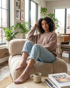 5-Pack Sheer Rose Embroidered Sock featuring a soft ribbed texture with semi-sheer panels, stretch ankle cuffs, and subtle rose embroidery accents, worn with rolled cuff jeans and a relaxed knit sweater while lounging on a cushioned chair in a bright modern living room, highlighting cozy everyday comfort and casual home styling.