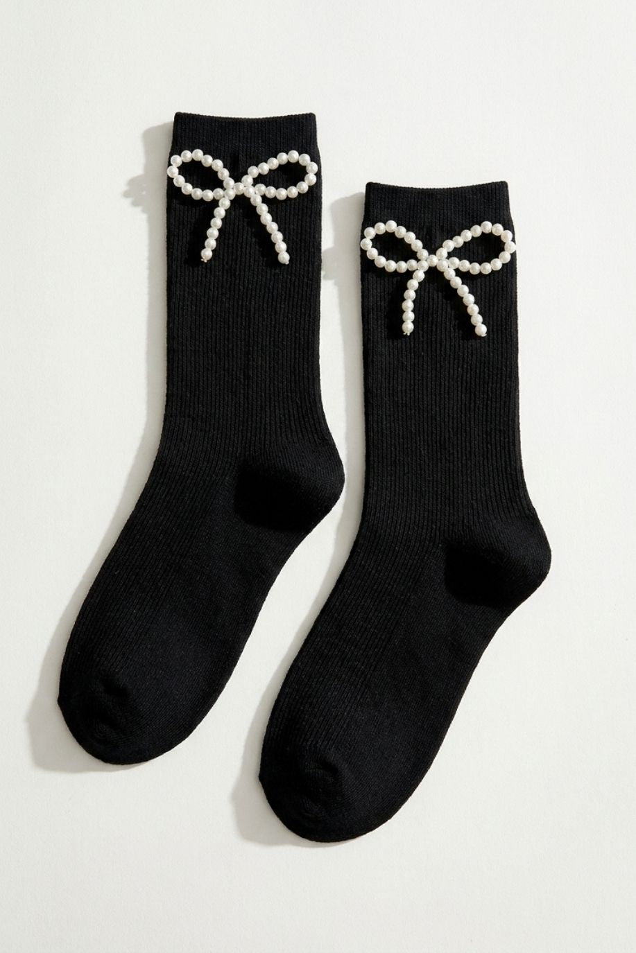Pearl Bow Classic Ribbed Crew Socks featuring a soft ribbed knit with a decorative pearl bow at the cuff, displayed as a flat lay in black on a clean white background, highlighting the classic crew length and polished statement detail.