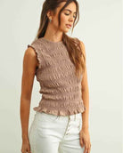 Sleeveless with All Over Smocking Top featuring a fitted all over smocked texture with soft ruffle sleeve trim and a ruffled hemline, styled with high waisted button front jeans in a side angled pose against a clean neutral backdrop, highlighting stretch comfort and flattering shape.