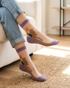 4-Pack Peacock Sheer Mesh Socks featuring lightweight transparent mesh fabric with embroidered peacock motifs and soft purple trim, worn indoors with rolled denim jeans in a bright living space, highlighting comfort and playful everyday styling.