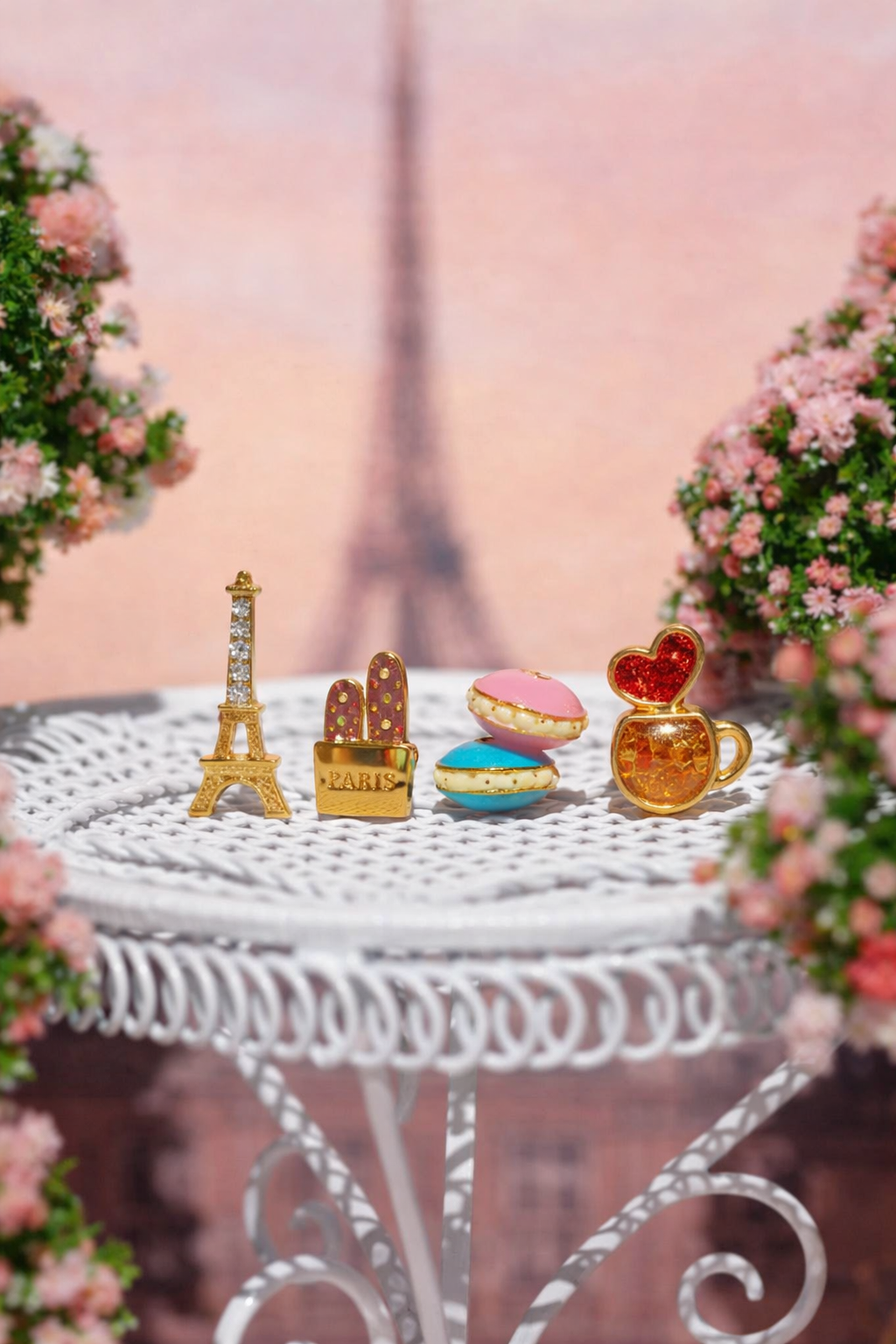 Café de Paris Stud Set, styled flat lay featuring Eiffel Tower, baguette bag, macarons, and coffee cup shaped studs arranged on a decorative table with a blurred Paris backdrop and floral accents.