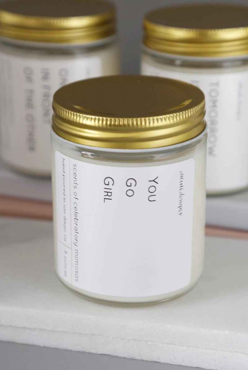 Glass candle jar with gold lid labeled 'You Go Girl', Love Classic high quality style.