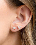 Remember Me Butterfly Studs featuring butterfly inspired crystal stones with a petite stud silhouette and polished metallic finish, worn on the ear in a close up portrait shot, highlighting subtle sparkle and delicate everyday elegance.