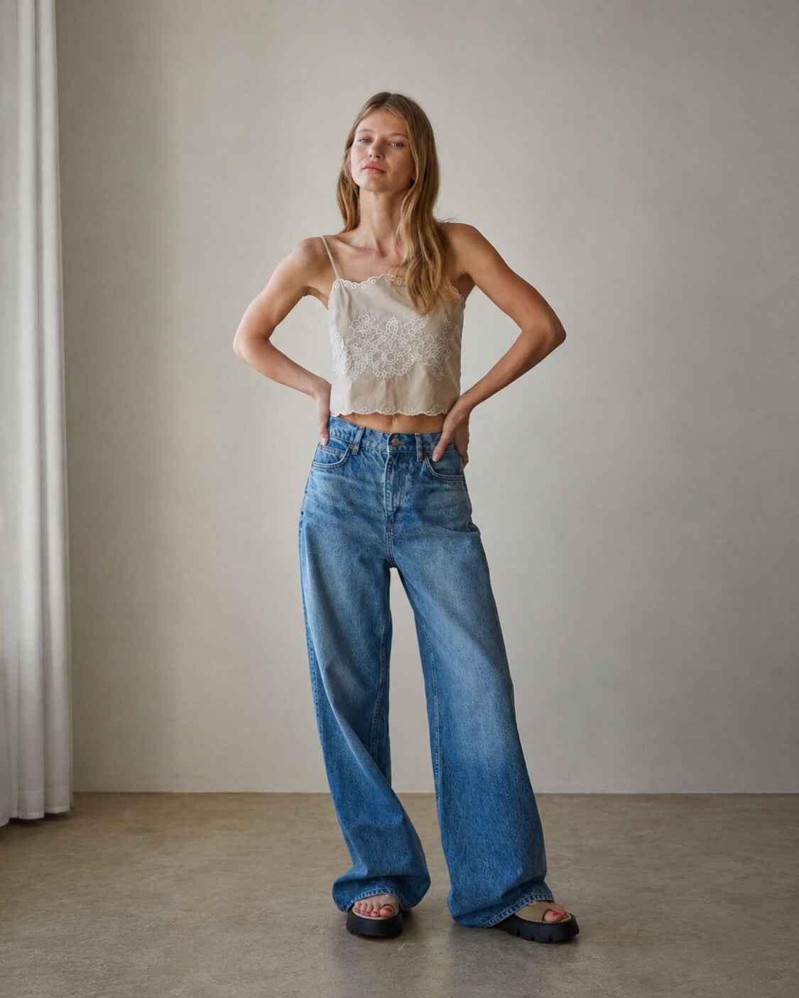 Floral Lace Work Sleeveless Top featuring intricate floral lace embroidery with a cropped sleeveless fit and scallop edge hem, styled with wide leg jeans during a full length standing pose in a minimalist indoor setting, highlighting the relaxed structure and breathable warm weather styling.