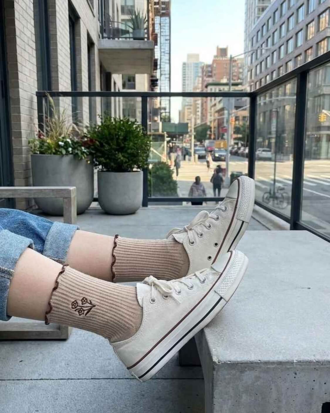 3-Pack Floral Bloom Ribbed Ruffle Crew Socks featuring ribbed crew socks with scalloped ruffle cuffs and floral embroidery near the ankle, worn with rolled cuff jeans and canvas sneakers on an outdoor balcony, highlighting casual street styling and soft everyday comfort.