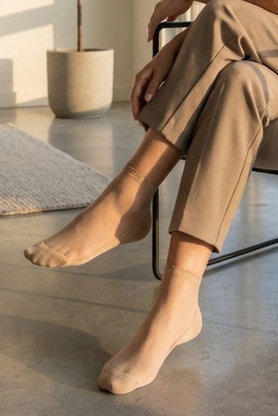 Glitter Rim Sheer Crew Socks, indoor lifestyle view showing transparent ankle socks with subtle shimmer cuff worn with relaxed trousers while seated in a softly lit modern living space.