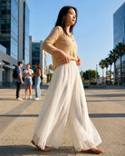 Chiffon Wide Leg Pant featuring a high-waist fit, sheer layered wide legs, and soft vertical pleating, worn with a button-front top and sandals in an open urban plaza, highlighting graceful movement and relaxed styling.
