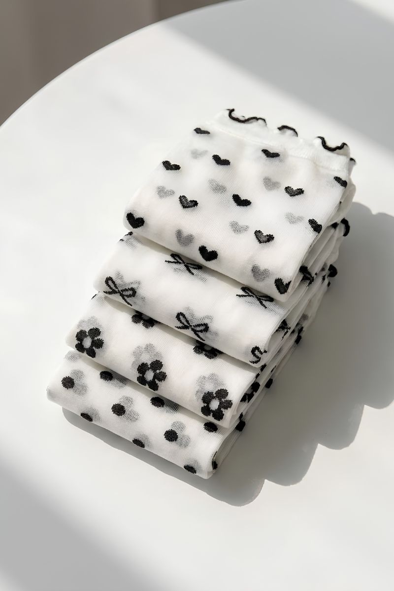 Bundled Pack Geo Print Ruffle Edge Sheer Socks featuring a soft sheer fabric with ruffle edge cuffs and mixed geometric prints, neatly folded into a stacked pile on a round white surface under natural light, emphasizing compact presentation and pattern detail.