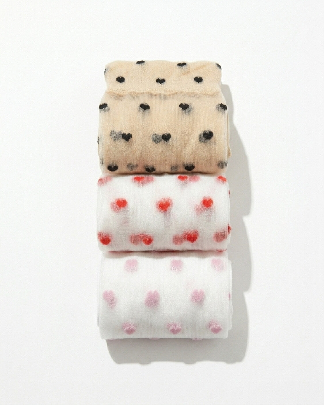 3-Pack Blushing Hearts Sheer Socks featuring folded sheer socks with black heart, red heart and soft dot patterns, stacked neatly on a bright studio surface, highlighting the compact bundle presentation and delicate transparent texture.