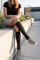 Heart Knee High Socks featuring a snug knee-high fit with repeated heart detailing and flexible fabric, styled with slip-on shoes while sitting outdoors to showcase casual wearability and expressive street-style appeal.