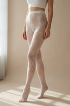 Sheer Floral Lace Tights featuring a delicate floral pattern and high waist fit, styled in a softly lit indoor setting near a window, highlighting the smooth stretch and elegant leg coverage.