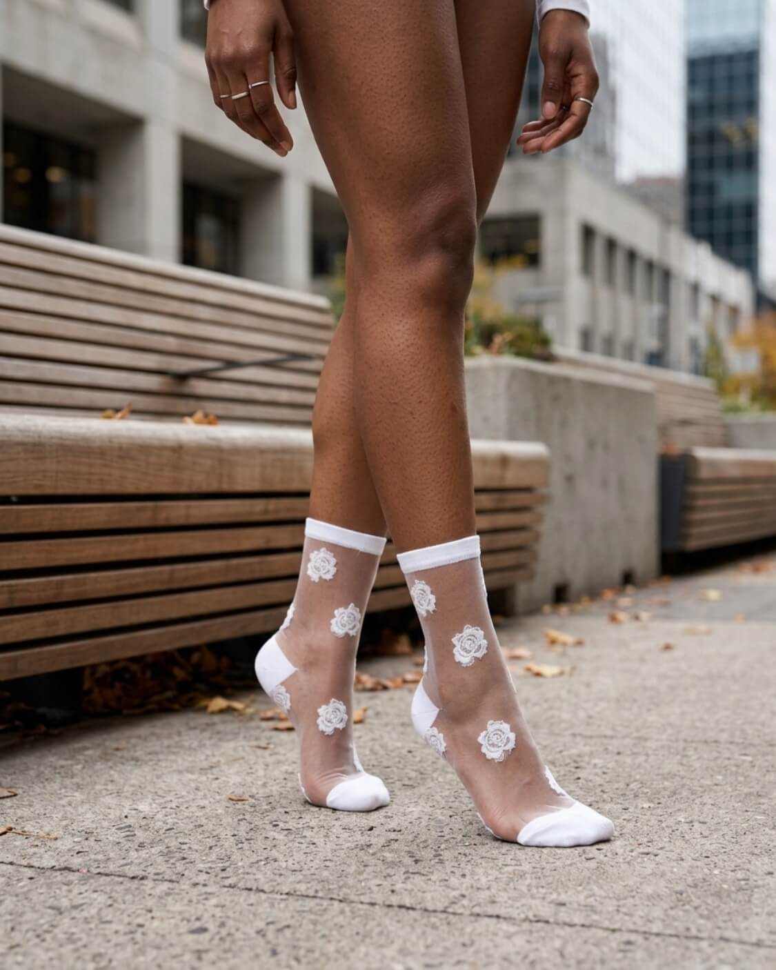 2-Pack Rosette Mesh Crew Socks featuring sheer mesh fabric with white rosette embroidery and matching white toe, heel, and cuff trim, worn during a relaxed walking pose on a modern city sidewalk, highlighting breathable comfort and delicate floral style for everyday wear.