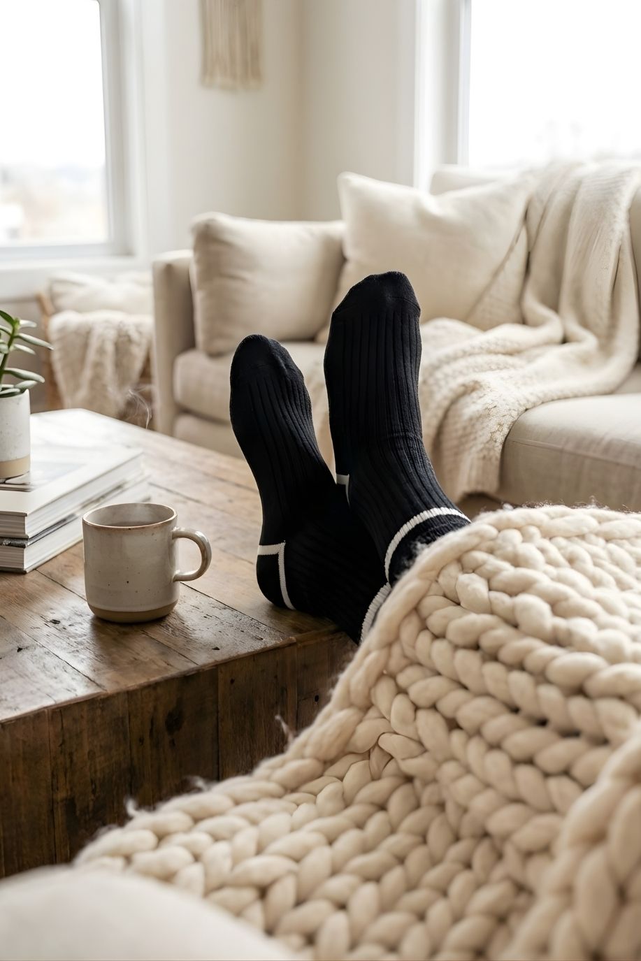 Classic Ribbed Crew Socks with Contrast Trim, black ribbed crew socks with white stripe accents worn while lounging on a sofa, styled with a cozy knit blanket and coffee table setting to evoke a relaxed, at-home feel.