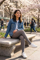 Lightweight Semi Opaque Tights in gray, featuring a lightweight semi-opaque knit and even coverage, styled with a denim jacket and sneakers, shown on a model seated on a park bench under blooming trees.