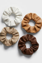 Set of four faux leather scrunchies in earthy neutral shades displayed in a grid layout, highlighting the smooth texture and structured gathered shape against a minimal white backdrop.