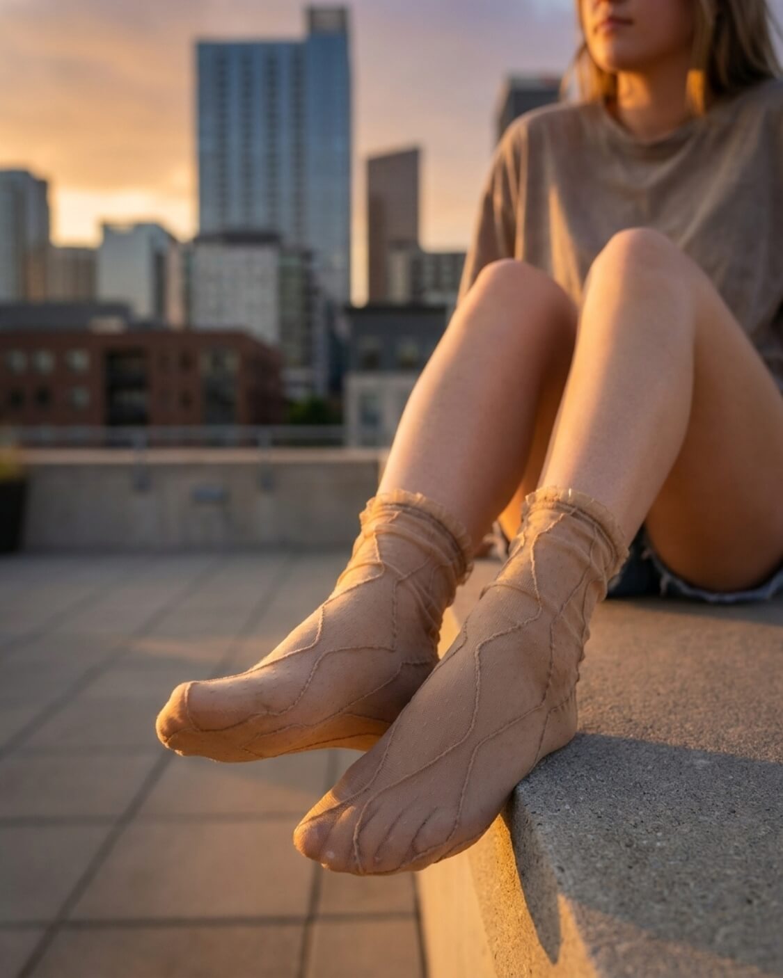 Bundled Packs Rosalie Lace Sheer Socks featuring nude sheer ankle socks with raised wavy lace texture and ruffled cuff trim, worn while seated on a rooftop ledge in warm sunset lighting, highlighting the lightweight translucent finish and delicate textured pattern.